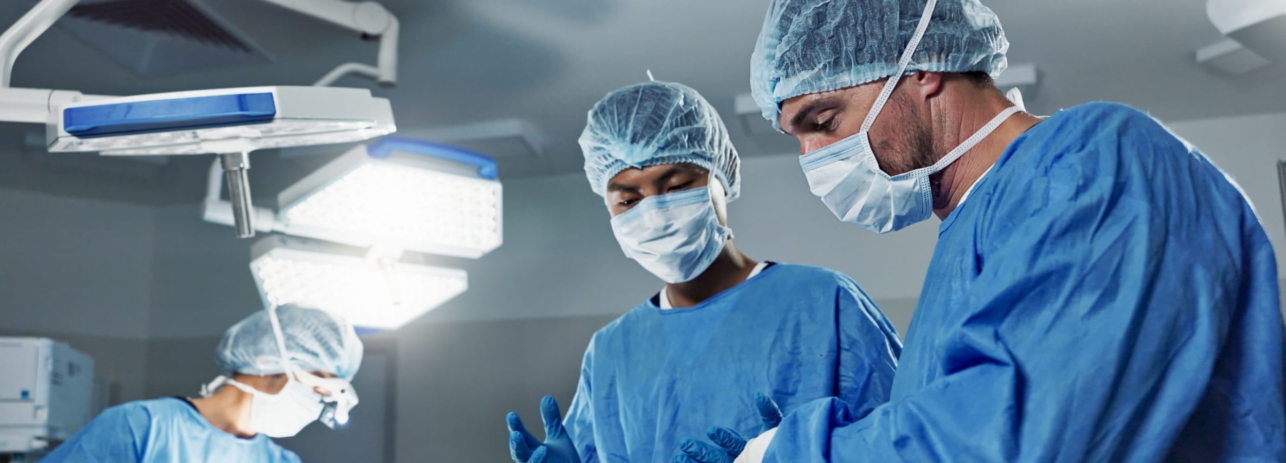 Equipo quirúrgico en quirófano durante una intervención de cirugía plástica, con cirujanos revisando información médica y realizando un procedimiento bajo iluminación quirúrgica.