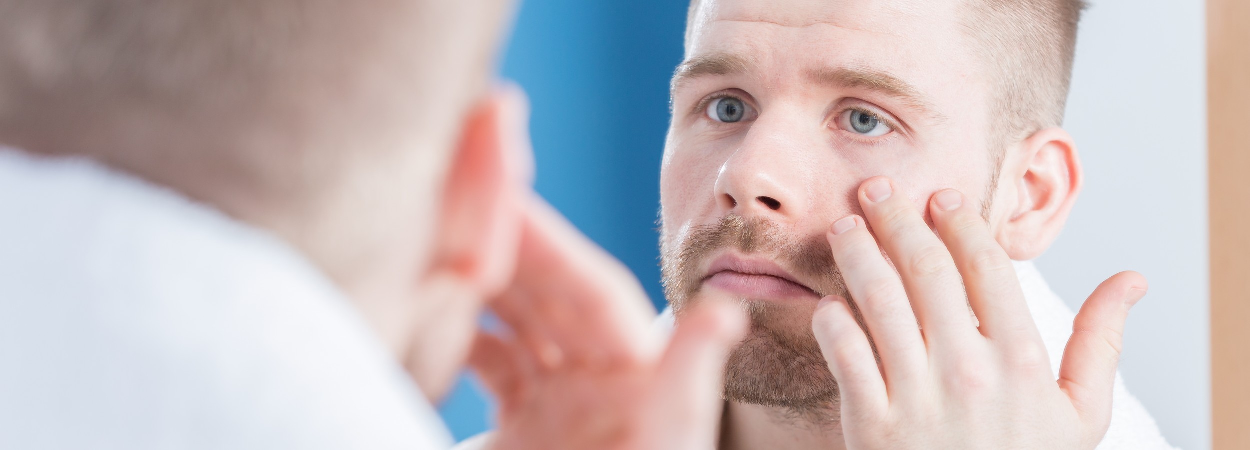 Hombre adulto en entorno clínico premium evaluando el contorno facial, imagen panorámica sin texto